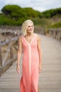 Eldery female walking along a wooden path near the beach., wearing a nice orange dress. Royalty Free Stock Photo