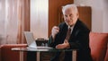 An eldery grandfather in glasses sitting by the laptop and looking in the camera Royalty Free Stock Photo