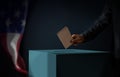 Election Day in United States of America Concept. Person Dropping a Ballot Card into the Vote Box. USA Flag hanging on the Wall. Royalty Free Stock Photo