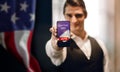 Election Day in United States Concept. Young Man presenting Online Vote on Mobile Phone Screen. USA Flag on the wall