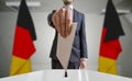 Election or referendum in Germany. Voter holds envelope in hand above ballot. German flags in background