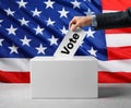 Election in USA. Man putting his vote into ballot box and American flag on background, closeup Royalty Free Stock Photo