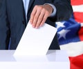 Election in USA. Man putting his vote into ballot box and American flag on background, closeup Royalty Free Stock Photo