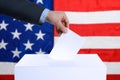 Election in USA. Man putting his vote into ballot box and American flag on background, closeup Royalty Free Stock Photo