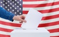 Elections, America. A human hand throws a ballot into the ballot box. American flag on the background. Election concept Royalty Free Stock Photo