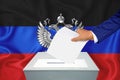 Elections in the country - voting at the ballot box. A man`s hand puts his vote into the ballot box. Flag dnr on background