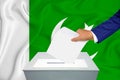 Elections in the country - voting at the ballot box. A man`s hand puts his vote into the ballot box. Flag Pakistan on background