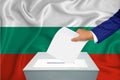 Elections in the country - voting at the ballot box. A man`s hand puts his vote into the ballot box. Flag Bulgaria on background
