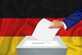 Elections in the country - voting at the ballot box. A man`s hand puts his vote into the ballot box. Flag germany on background
