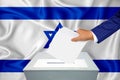 Elections in the country - voting at the ballot box. A man`s hand puts his vote into the ballot box. Flag Israel on background