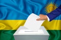 Elections in the country - voting at the ballot box. A man`s hand puts his vote into the ballot box. Flag Rwanda on background Royalty Free Stock Photo