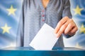 Elections In European Union. The Hand Of Woman Putting Her Vote In The Ballot Box. EU Flag In The Background
