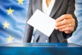 Elections In European Union. The Hand Of Woman Putting Her Vote In The Ballot Box. EU Flag In The Background