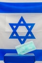 Israeli Elections. Medical face mask in a box for ballot in election on Israel flag background.