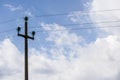 Electric cables sustained by a concrete pole, against the blue sky with white clouds