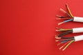 Electric cables with wires on red background, flat lay. Space for text Royalty Free Stock Photo