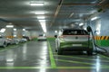 An electric car is being charged with a charging cable in a multilevel parking garage filled with parked cars, Electric car