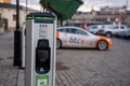 Electric car charging point with Tesla car plugged in decorated with Bitcoin and Nasdaq logotypes.