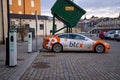 Electric car charging point with Tesla car plugged in decorated with Bitcoin and Nasdaq logotypes.