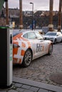 Electric car charging point with Tesla car plugged in decorated with Bitcoin and Nasdaq logotypes.