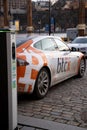 Electric car charging point with Tesla car plugged in decorated with Bitcoin and Nasdaq logotypes. Bitcoin and cryptocurrency