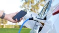 Electric car or ev is charging at station . man use the white power cable and plug on nature background. eco and clean energy Royalty Free Stock Photo