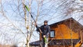 Electric chain pruner with a telescopic pole close up. Winter tree pruning. A man gardener standing on a stepladder cuts branches