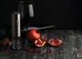 The electric corkscrew stands on a dark wood background. Next to it is a cut pomegranate, a bottle and a glass of wine. Dark