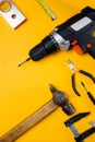 Electric drill and drill bits on a yellow background. Hammer drill or screwdriver flat lay. Top view of professional instrument.