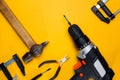 Electric drill, hummer, wire cutters and clamp on a yellow background. Hammer drill or screwdriver flat lay. Top view of