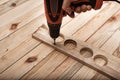 Electric drill screwdriver in male hand. Tightening screw, processing workpiece on light brown wooden table. Close up