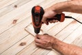 Electric drill screwdriver in male hand. Tightening screw, processing workpiece on light brown wooden table