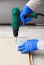 Electric Drill works in handyman hands at home. Male hands in gloves using electric drill tool to assemble and repair furniture.