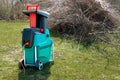 Electric garden shredder with weathered lawn and pile of cut tree branches in the background. Cleanup around the house