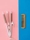 Electric hair curler and wooden comb on a blue and pink background. Royalty Free Stock Photo