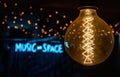 Electric incandescent lamp on the background of half-blurred neon music-space inscription