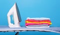 Electric iron and pile of clothes on ironing board Royalty Free Stock Photo