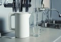 Electric kettle white matte surface, kitchen fragment. Glass and faucet of filtered water in the background