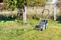 An electric lawn mower stands on a green lawn in a garden area in bright sunlight