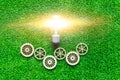 Electric light bulb, gears on the background of artificial green grass. Royalty Free Stock Photo