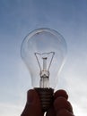 Electric light bulb in hand against the blue sky during a sunny evening Royalty Free Stock Photo