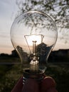 Electric light bulb in hand against the sun during the evening Royalty Free Stock Photo