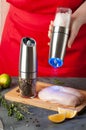 Electric mill with coarse salt in a woman`s hand. Chicken fillet salt. Nearby there is a second pepper mill for spices. Herbs and Royalty Free Stock Photo