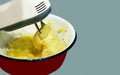 An electric mixer in a metal red plate whips up yellow baking dough, on a gray background. Close-up of a mixer mixing cake batter.