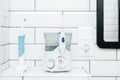 Electric oral irrigator and a rechargeable toothbrush are in the white tiled bathroom, next to the mirror. Royalty Free Stock Photo