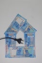 The electric plug lies on the banknotes laid out in the form of a house, electricity savings, energy crisis. expensive