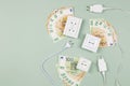 Electric power plugs and electric sockets with Euro banknotes on light green background. Electricity cost and expensive Royalty Free Stock Photo