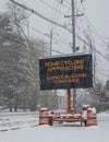 Electric road traffic mobile sign by the side of a snow covered road with snow falling warning of BOMB CYCLONE approaching, expect