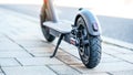 Electric scooter parked on tiled stone pavement - closeup detail on rear wheel