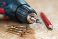 Electric screwdriver, self drilling screws and carpenter pencil lying on chip board. Blurred background
